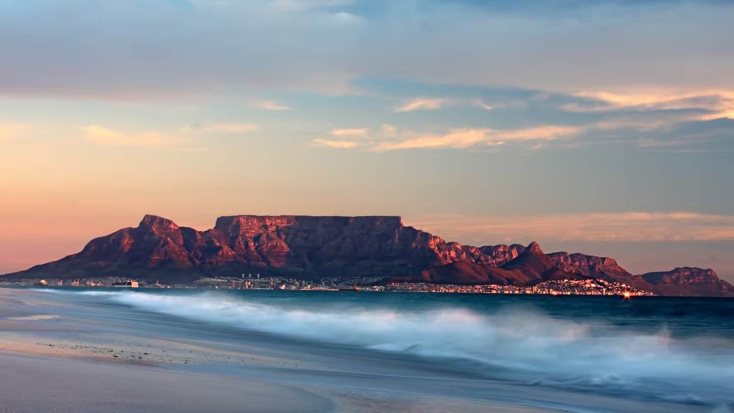 Table Mountain at dusk, seen across the ocean from a beach, its flat summit glowing in the last light
